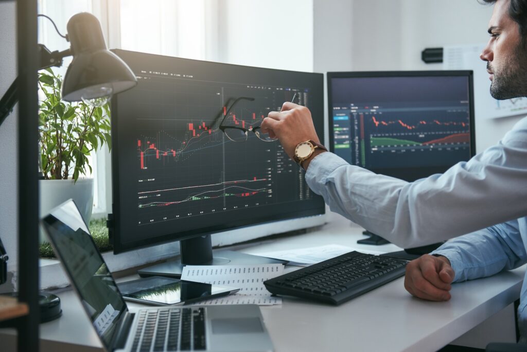 Forex market. Young trader is pointing at graphs on computer screen and analyzing data while working
